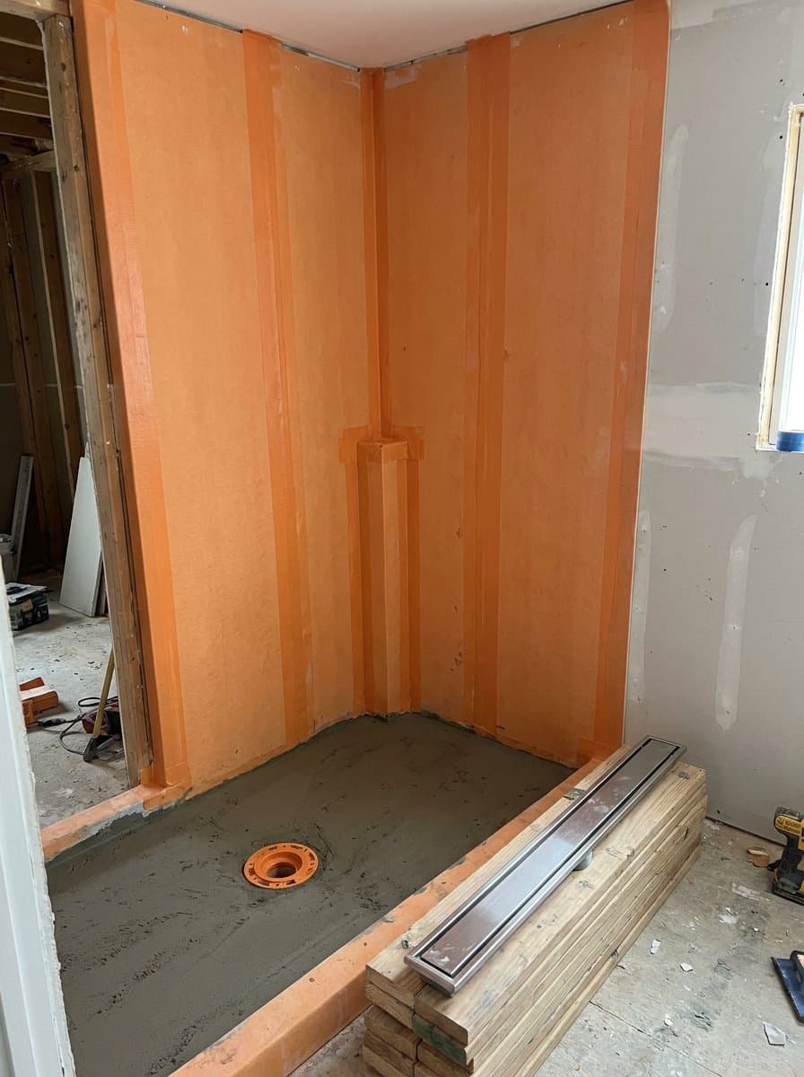 Shower corner covered in bonded orange waterproofing membrane with taped seams